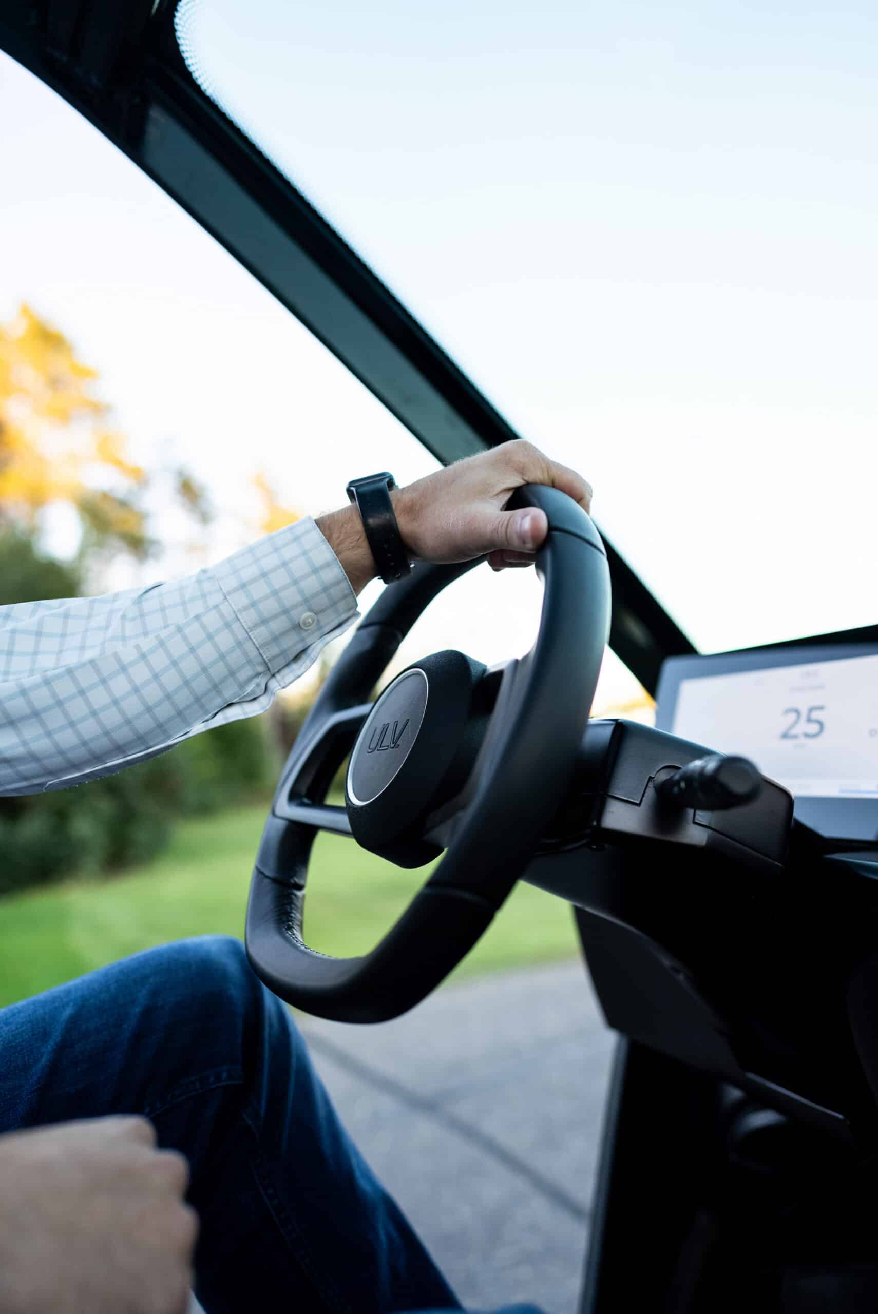Stylistic image of a hand on the steering wheel of a ULV 322 and a partial view of the electronic dashboard showing 25mph